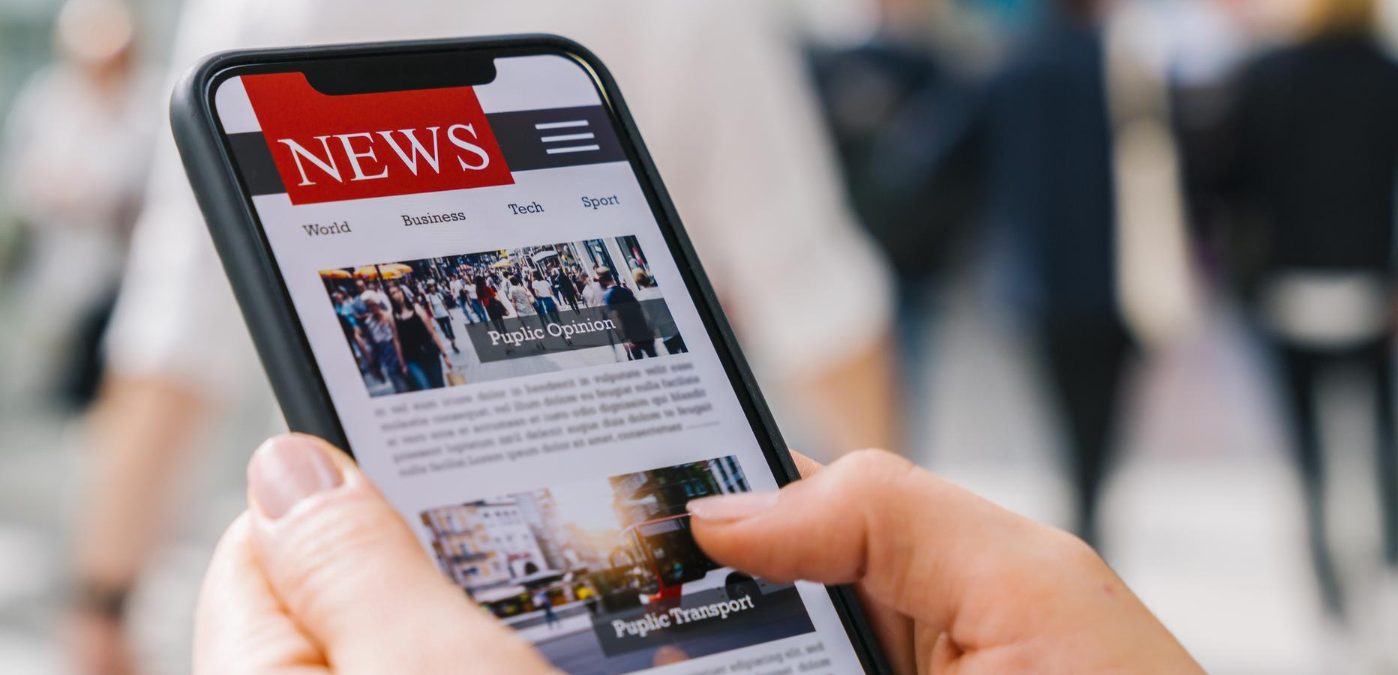 Reading news articles on a smartphone screen application, with a hand holding the smart device, showcasing a mockup of a website newspaper portal on the internet