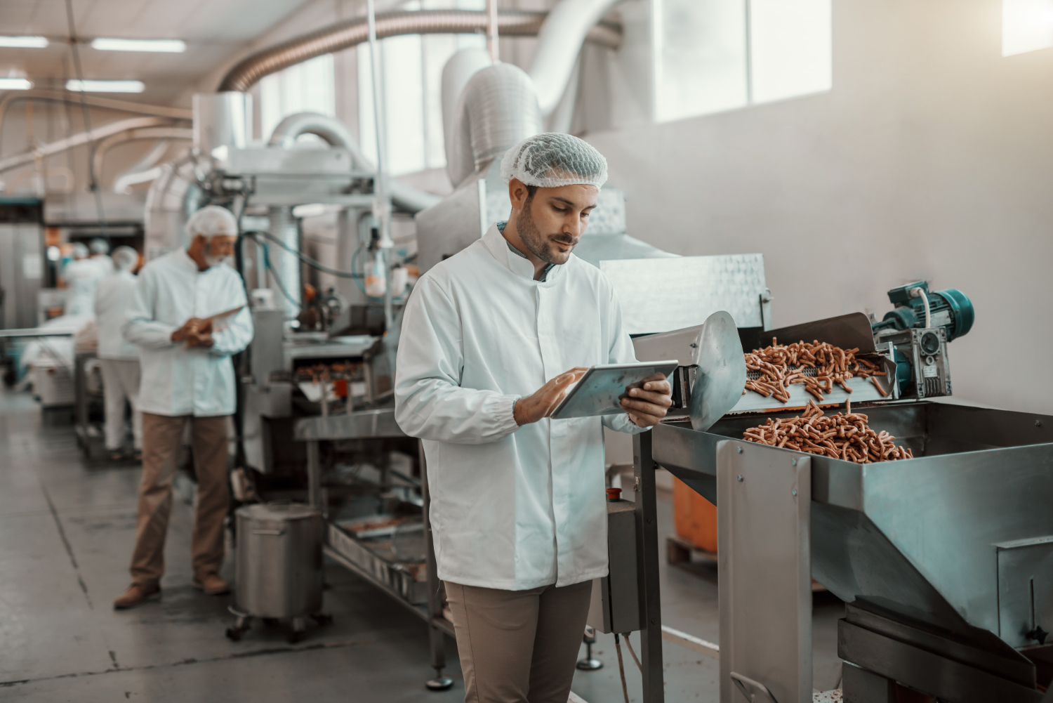 young-caucasian-serious-supervisor-evaluating-quality-food-food-plant-while-holding-tablet-man-is-dressed-white-uniform-having-hair-net